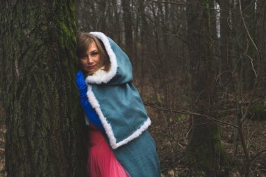 Mantolu bir kadın ağaca yaslanmış. Pelerinli fantezi kostümlü yetişkin bir kadın. sihirli sonbahar