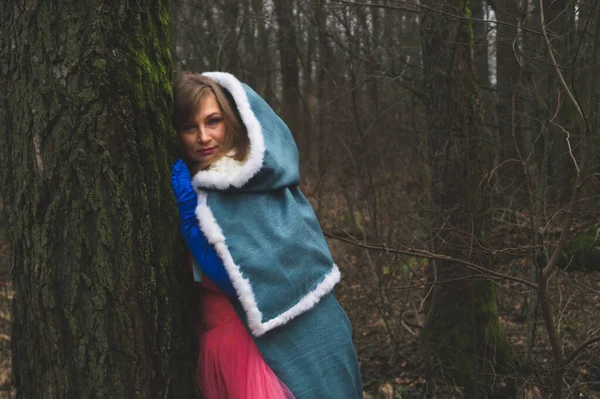 Mantolu bir kadın ağaca yaslanmış. Pelerinli fantezi kostümlü yetişkin bir kadın. sihirli sonbahar