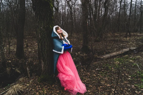 Mantolu bir kadın ağaca yaslanmış. Pelerinli fantezi kostümlü yetişkin bir kadın. sihirli sonbahar