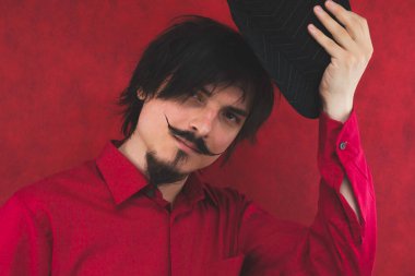 Genç adam şapkasını çıkarıyor. Kırmızı arkaplanda erkek portresi