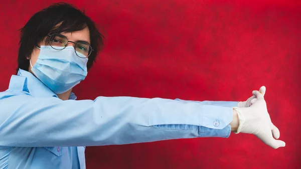 Young man in a medical mask with gloves and glasses on a red background. male portrait. virus protection measures