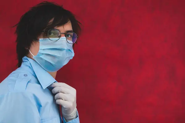 Young man in a medical mask with gloves and glasses on a red background. male portrait. virus protection measures