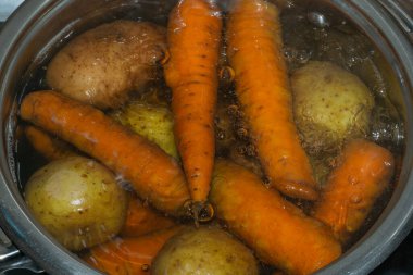 Sıcak suyla dolu bir tencerede patates ve havuç kaynıyor. Salata için sebze hazırlıyorum.