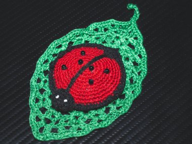 Tığ işi yaprağın üzerine örülmüş oyuncak uğur böceği. El yapımı iğnelik. Yakın çekim.