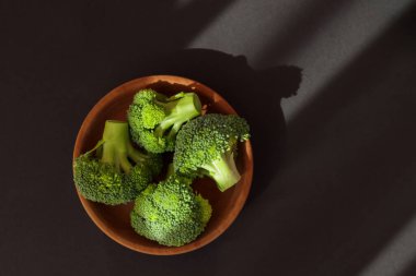 Broccoli in wooden bowl, on dark background, top view