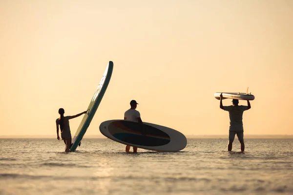 Three friends stands with sup boards in hands — Stock Photo, Image