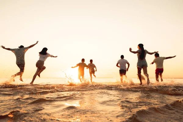 Велика група друзів або велика сім'я біжить на пляжі заходу сонця — стокове фото