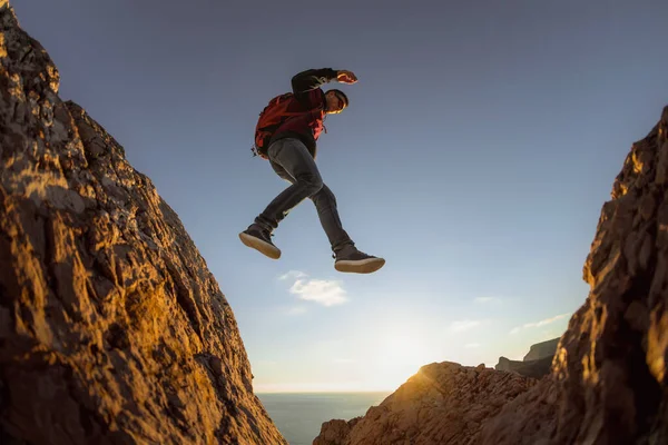 Sportowy facet z plecakiem skacze z kamienia do kamienia — Zdjęcie stockowe
