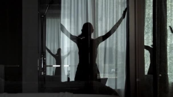 Young woman doing star jumps in the living room. Slow motion silhouette reflection in the glass window. Healthy and active lifestyle. — Stock Video