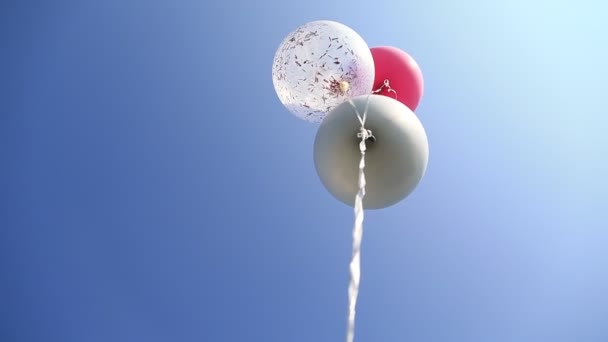 Три разноцветных гелиевых шарика, плавающих в голубом небе. День рождения. — стоковое видео