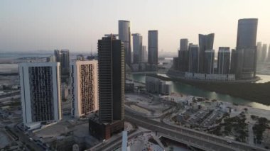 Abu Dabi 'de günbatımı, Al Reem adasındaki hava manzarası denizdeki mangrovlar arasında modern gökdelenlerle çevrili.