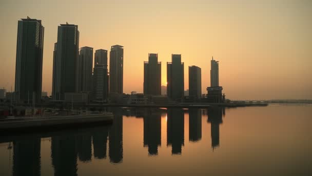 Zonsopgang op het eiland Al Reem in Abu Dhabi, stadsgezicht. Silhouetten van de hoogbouw moderne gebouwen met de zon die achter hen opkomt. — Stockvideo