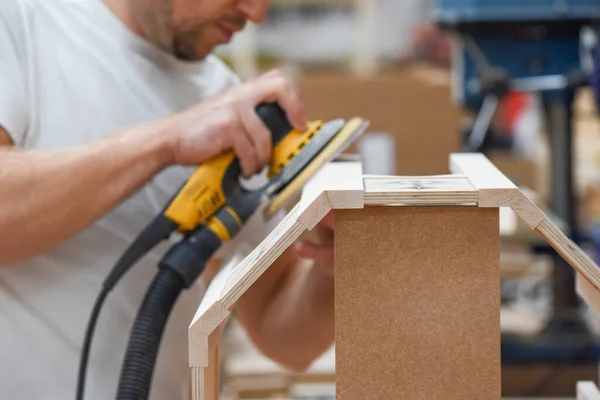 A man using a power tool electric sander to craft wood in the carpentry trade