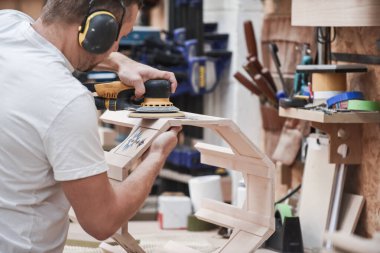 Marangozluk işinde odun yapmak için elektrikli zımpara makinesi kullanan bir adam.