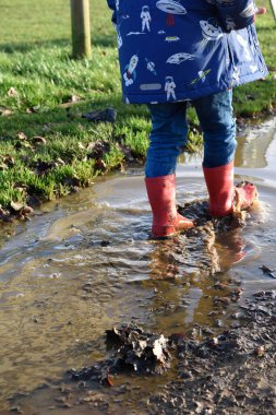 Kırmızı çizmeli çocuk su birikintilerinde sıçrıyor.