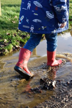 Kırmızı çizmeli çocuk su birikintilerinde sıçrıyor.