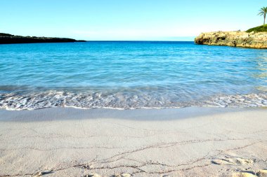 Güzel, boş bir sahil. Beyaz kum ve açık mavi okyanus suyu kıyıda.