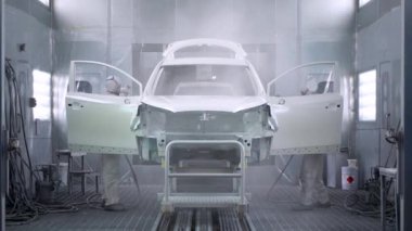 İki adam sprey boya kabinine araba boyuyor. Araba üretimi.