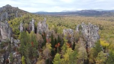Kayalık tepelerin ve sarı yeşil sonbahar ormanlarının havadan görünüşü. Bir sonbahar günü, dağların üzerinden peyzaj uçuşu. Rusya 'da Ural Sırtı İlham verici doğa
