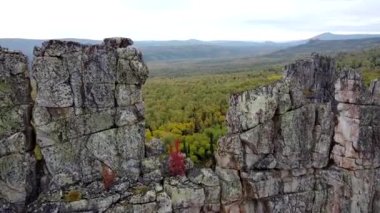 Kayalık tepelerin ve sarı yeşil sonbahar ormanlarının havadan görünüşü. Bir sonbahar günü, dağların üzerinden peyzaj uçuşu. Rusya 'da Ural Sırtı İlham verici doğa