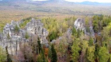 Kayalık tepelerin ve sarı yeşil sonbahar ormanlarının havadan görünüşü. Bir sonbahar günü, dağların üzerinden peyzaj uçuşu. Rusya 'da Ural Sırtı İlham verici doğa