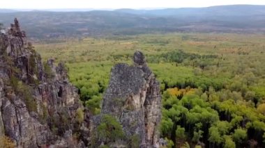 Kayalık tepelerin ve sarı yeşil sonbahar ormanlarının havadan görünüşü. Bir sonbahar günü, dağların üzerinden peyzaj uçuşu. Rusya 'da Ural Sırtı İlham verici doğa