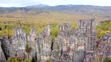 Kayalık tepelerin ve sarı yeşil sonbahar ormanlarının havadan görünüşü. Bir sonbahar günü, dağların üzerinden peyzaj uçuşu. Rusya 'da Ural Sırtı İlham verici doğa