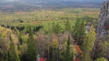 Kayalık tepelerin ve sarı yeşil sonbahar ormanlarının havadan görünüşü. Bir sonbahar günü, dağların üzerinden peyzaj uçuşu. Rusya 'da Ural Sırtı İlham verici doğa