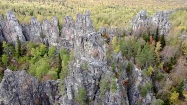 Kayalık tepelerin ve sarı yeşil sonbahar ormanlarının havadan görünüşü. Bir sonbahar günü, dağların üzerinden peyzaj uçuşu. Rusya 'da Ural Sırtı İlham verici doğa