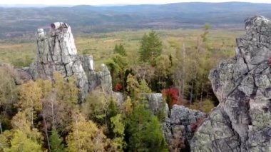 Kayalık tepelerin ve sarı yeşil sonbahar ormanlarının havadan görünüşü. Bir sonbahar günü, dağların üzerinden peyzaj uçuşu. Rusya 'da Ural Sırtı İlham verici doğa