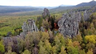 Kayalık tepelerin ve sarı yeşil sonbahar ormanlarının havadan görünüşü. Bir sonbahar günü, dağların üzerinden peyzaj uçuşu. Rusya 'da Ural Sırtı İlham verici doğa