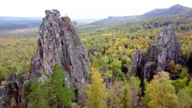 Kayalık tepelerin ve sarı yeşil sonbahar ormanlarının havadan görünüşü. Bir sonbahar günü, dağların üzerinden peyzaj uçuşu. Rusya 'da Ural Sırtı İlham verici doğa