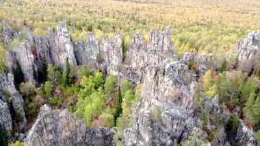 Kayalık tepelerin ve sarı yeşil sonbahar ormanlarının havadan görünüşü. Bir sonbahar günü, dağların üzerinden peyzaj uçuşu. Rusya 'da Ural Sırtı İlham verici doğa