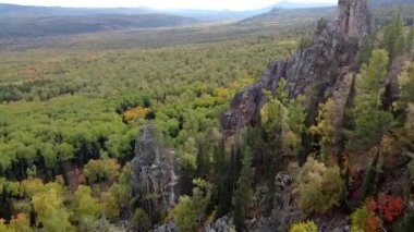 Kayalık tepelerin ve sarı yeşil sonbahar ormanlarının havadan görünüşü. Bir sonbahar günü, dağların üzerinden peyzaj uçuşu. Rusya 'da Ural Sırtı İlham verici doğa