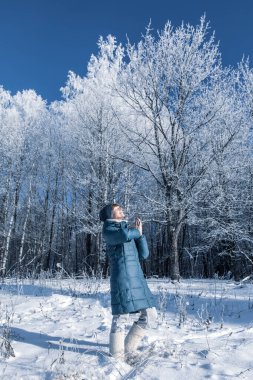 Genç kadın kış ormanında dinleniyor. Beyaz karlı arka planda mavi ceket