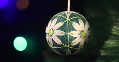 Yeni yılın yumuşak el yapımı oyuncağı yeşil ladin dalında sallanıyor. Arka plandaki Noel ışıkları yanıp sönüyor.