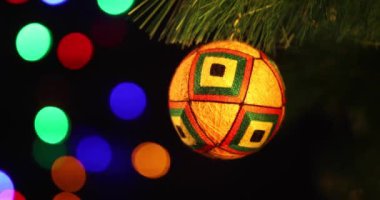 Yeni yılın yumuşak el yapımı oyuncağı yeşil ladin dalında sallanıyor. Arka plandaki Noel ışıkları yanıp sönüyor.