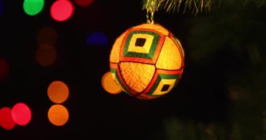 Yeni yılın yumuşak el yapımı oyuncağı yeşil ladin dalında sallanıyor. Arka plandaki Noel ışıkları yanıp sönüyor.