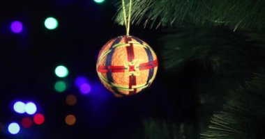 Yeni yılın yumuşak el yapımı oyuncağı yeşil ladin dalında sallanıyor. Arka plandaki Noel ışıkları yanıp sönüyor.