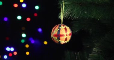 Yeni yılın yumuşak el yapımı oyuncağı yeşil ladin dalında sallanıyor. Arka plandaki Noel ışıkları yanıp sönüyor.