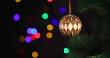 Yeni yılın yumuşak el yapımı oyuncağı yeşil ladin dalında sallanıyor. Arka plandaki Noel ışıkları yanıp sönüyor.