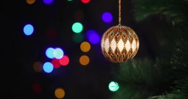 Yeni yılın yumuşak el yapımı oyuncağı yeşil ladin dalında sallanıyor. Arka plandaki Noel ışıkları yanıp sönüyor.