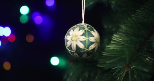 新年のクリスマスの柔らかい手作りのおもちゃは緑のトウヒの枝に群がっています 背景のクリスマスライトが点滅している — ストック動画