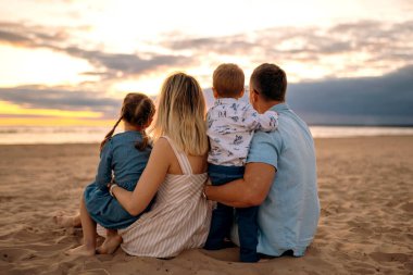 Mutlu bir aile. Anne, baba ve iki çocuk. Bir kız ve erkek bebek kumsalda kumsalda oturup altın gün batımını izliyorlar. Yüksek kalite fotoğraf