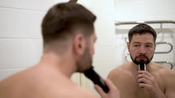 Jovem Caucasiano Homem Aparando Sua Barba Banheiro Reflexo Espelho Imagens — Vídeo de Stock