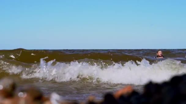 Vista de cerca de las olas que golpean en la playa. Los chicos corren en el agua — Vídeo de stock