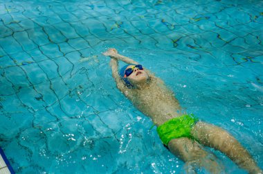 Gözlüklü küçük beyaz çocuk havuzda sırt üstü yüzüyor. Yüksek kalite fotoğraf