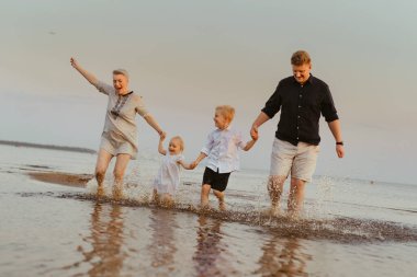 Kafkasyalı güzel bir aile gün batımında denizde koşuyor. Çocuklarla yaz tatili. Yüksek kalite fotoğraf