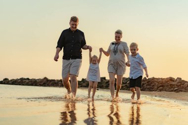 Kafkasyalı güzel bir aile gün batımında denizde koşuyor. Çocuklarla yaz tatili. Yüksek kalite fotoğraf