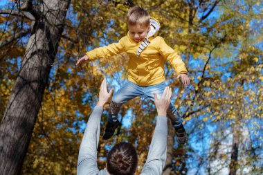 Genç baba, yakışıklı ve küçük oğlunu sonbahar parkında havaya fırlatıyor. Yüksek kalite fotoğraf
